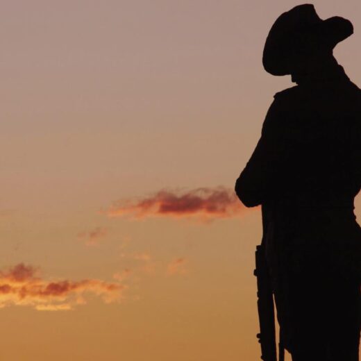 Silhouette of a cowboy in a hat with a rifle, standing against an orange sunset.
