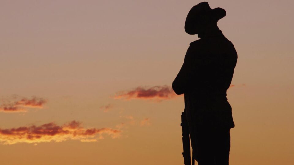 Silhouette of a cowboy in a hat with a rifle, standing against an orange sunset.