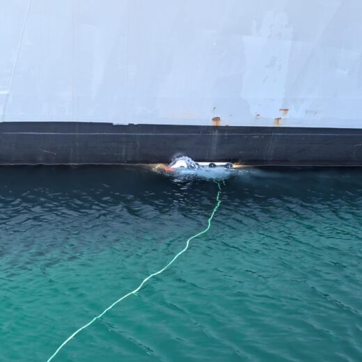 Swimmer in turquoise water next to the hull of a large white boat, connected by a green rope.