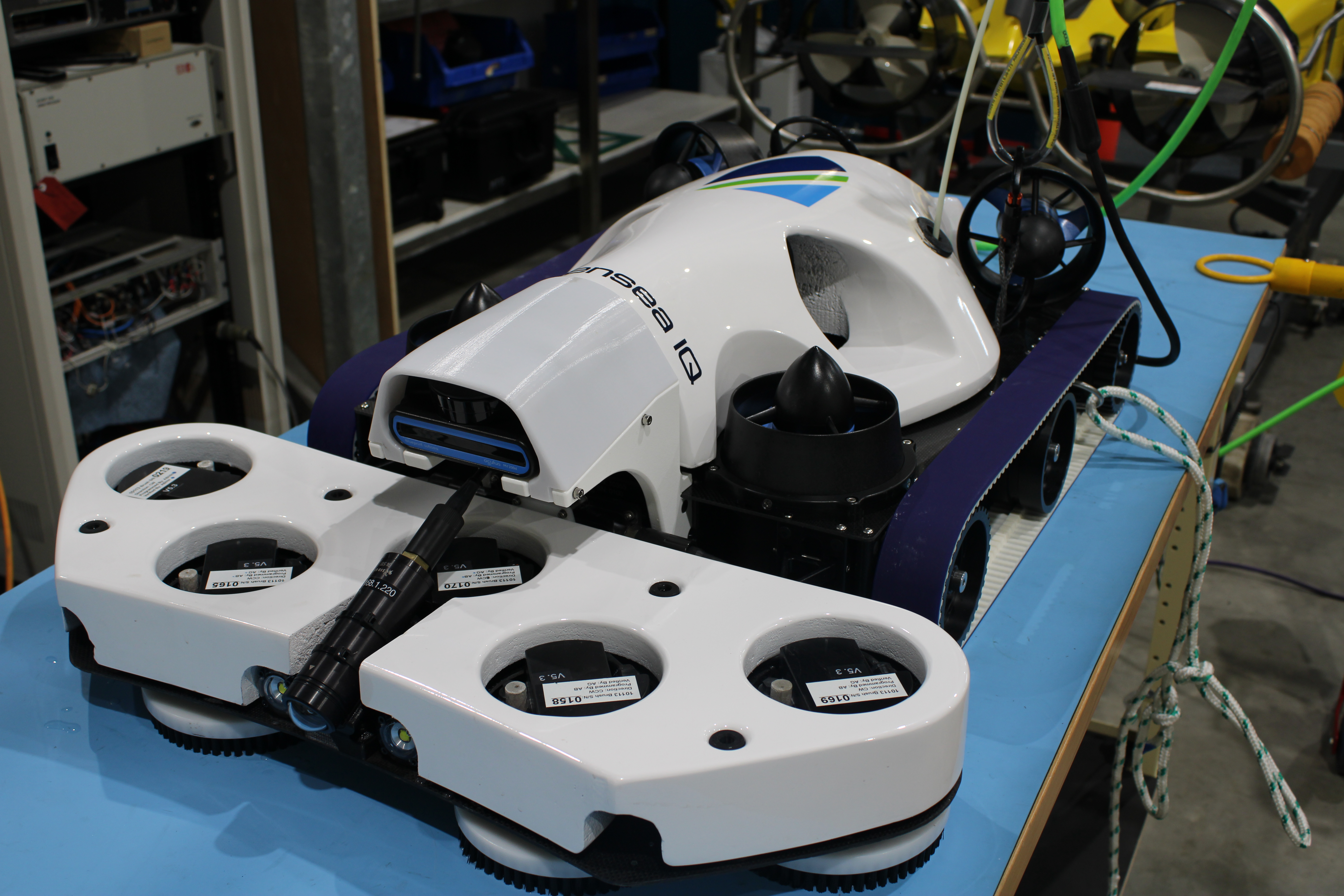 White streamlined ROV/underwater vehicle on a lab test rig with multiple thruster pods and cables visible behind it.