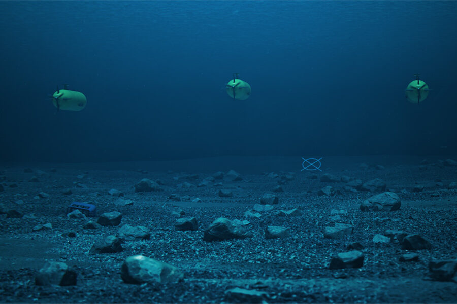 Three yellow underwater autonomous vehicles hover above a rocky seabed in blue water.