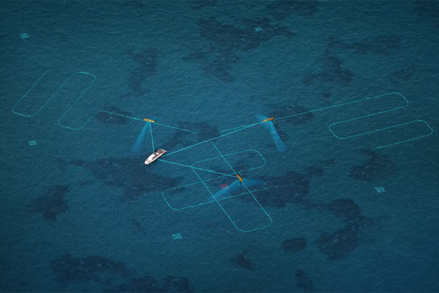 Aerial view of a small white boat with blue sails gliding over turquoise water, surrounded by aqua geometric marks drawn on the sea surface.