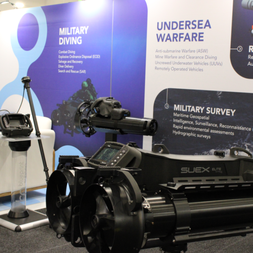 Exhibit booth with blue panels titled ‘Military Diving’ and ‘Undersea Warfare’, showing a large black marine deployment device and control console on display.