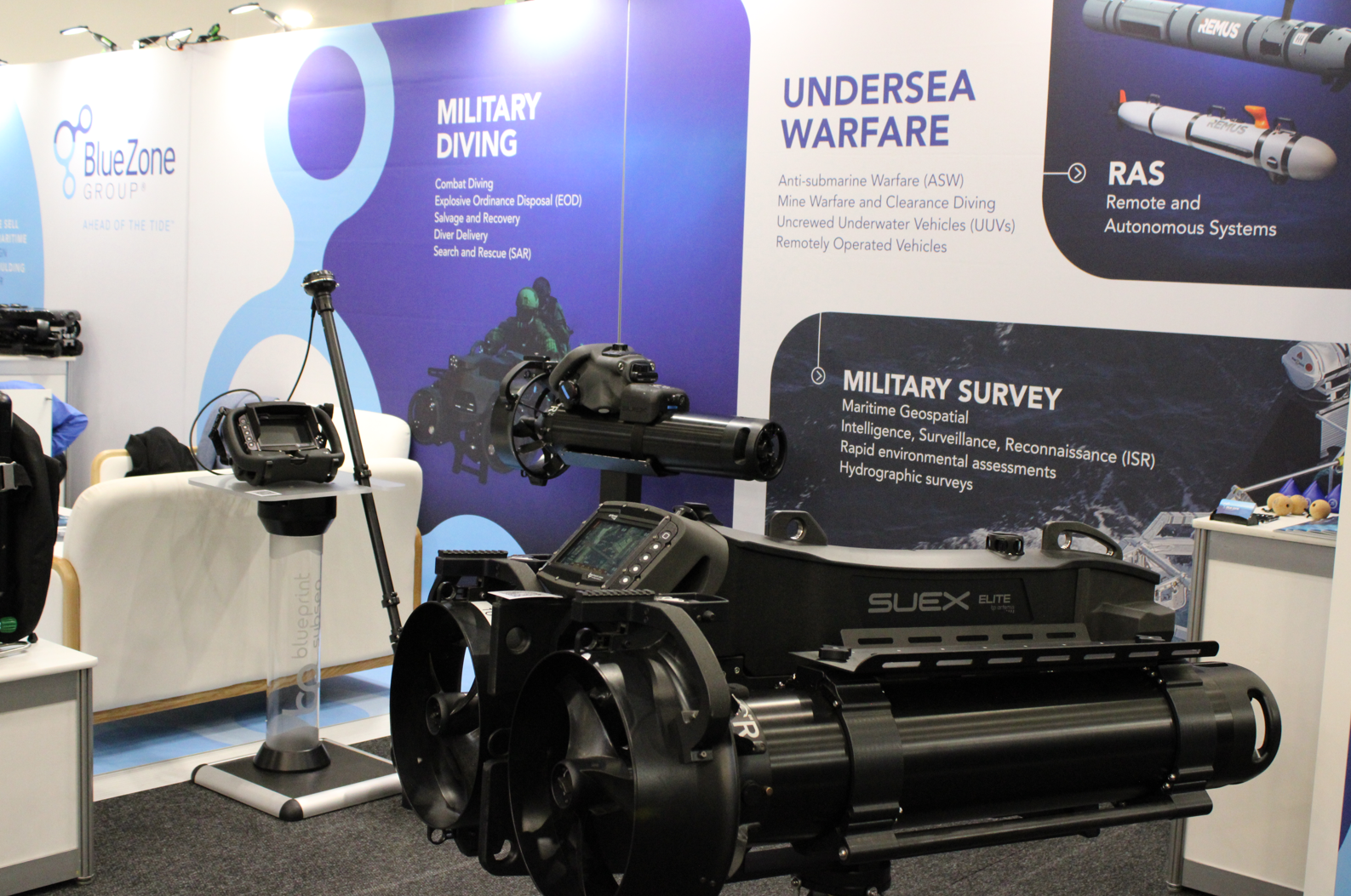 Exhibit booth with blue panels titled ‘Military Diving’ and ‘Undersea Warfare’, showing a large black marine deployment device and control console on display.