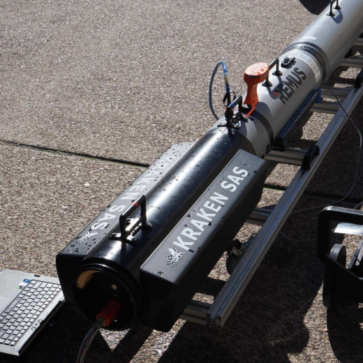 Remote-operated underwater vehicle (REMUS) and equipment on a rack with a laptop on a paved surface, connected by cables for testing/training.