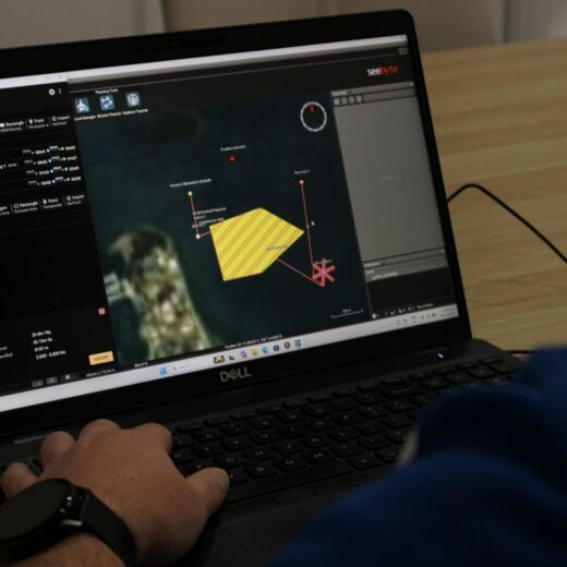 Hands on a Dell laptop displaying a multi-panel data visualization dashboard with a yellow polygon and red connection lines on screen