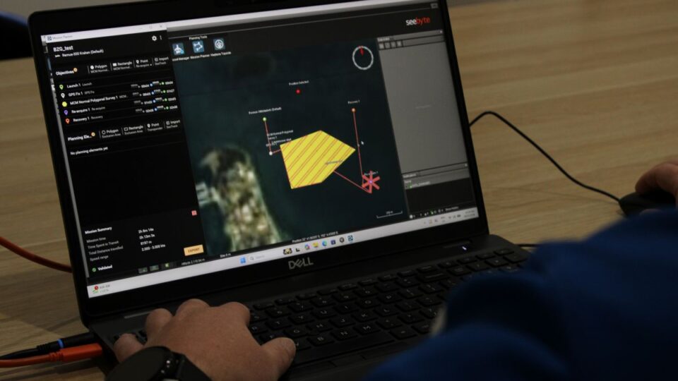 Hands on a Dell laptop displaying a multi-panel data visualization dashboard with a yellow polygon and red connection lines on screen