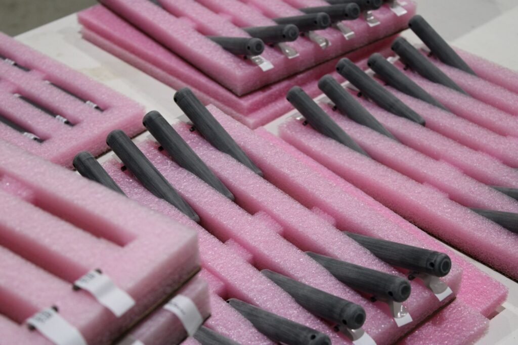 Gray cylindrical components laid in zigzag rows within pink foam packaging inserts for shipment/storage.