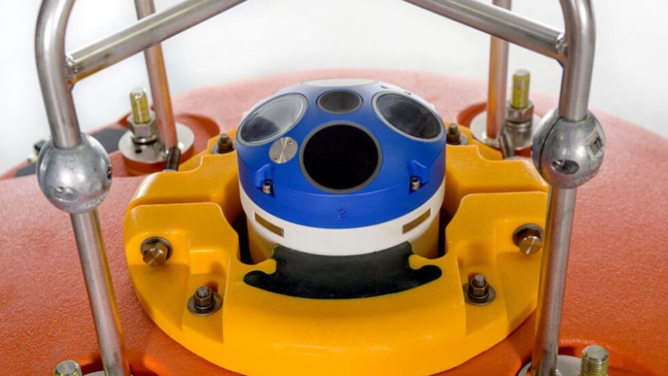 Blue circular sensor housing mounted in a yellow robotic base, surrounded by metal framing bars (industrial sensor setup).