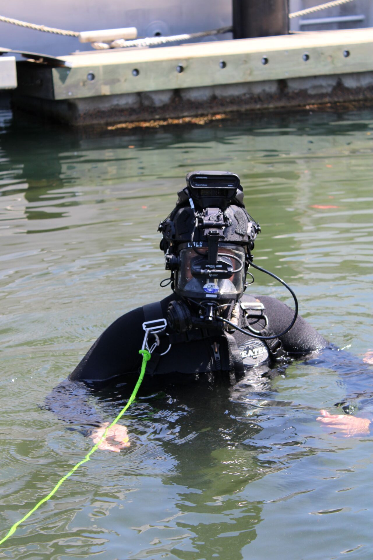 IMG_0751- resized - BlueZone Group SCUBA diver in a black wetsuit and gear in water near a wooden dock, connected to a bright green tether line.